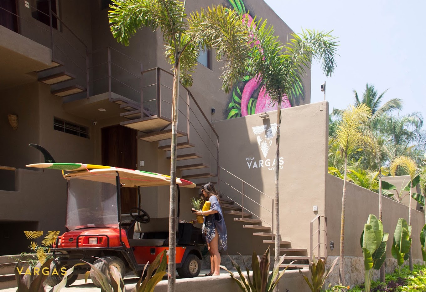The exterior of Villa Vargas Sayulita: stucco walls, an open-tread exterior staircase, a tropical mural, surfboards and a golf cart parked on the property