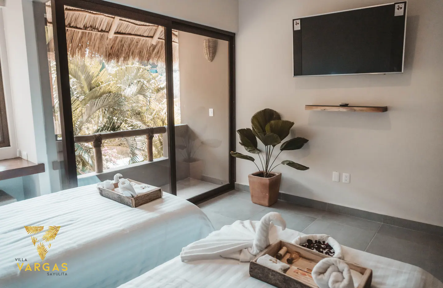 The upstairs twin bedroom at Villa Vargas Sayulita looking back at the television wall, the potted fan palm and the sliding doors onto the upper terrace