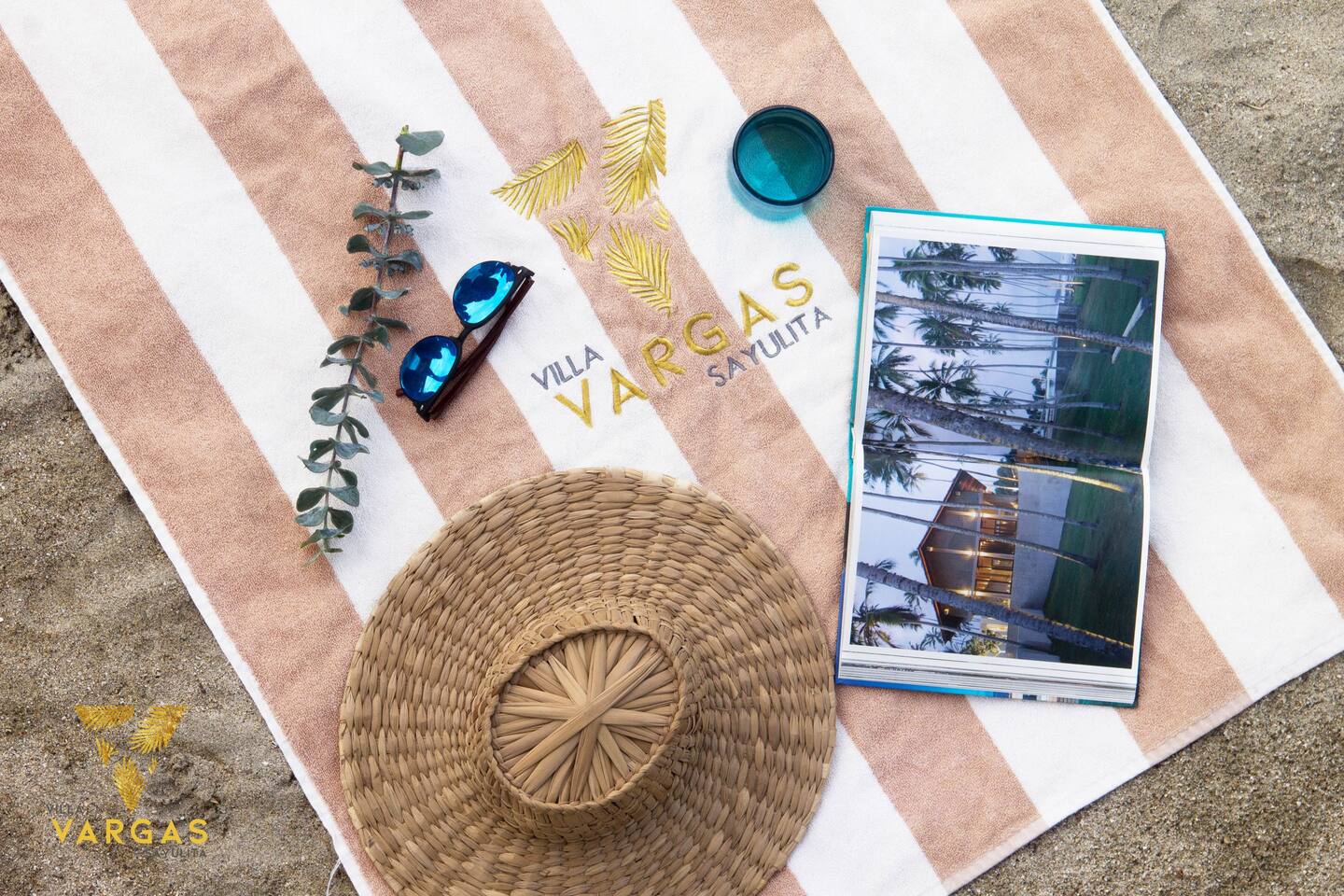 Beach essentials laid out on a Villa Vargas towel: a woven hat, sunglasses and a book