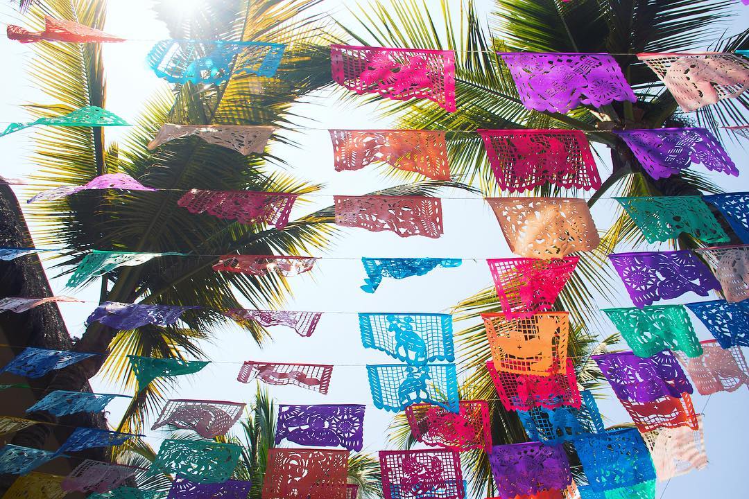 Papel picado banners strung above the outdoor terrace at Villa Vargas Sayulita against palm fronds and blue sky