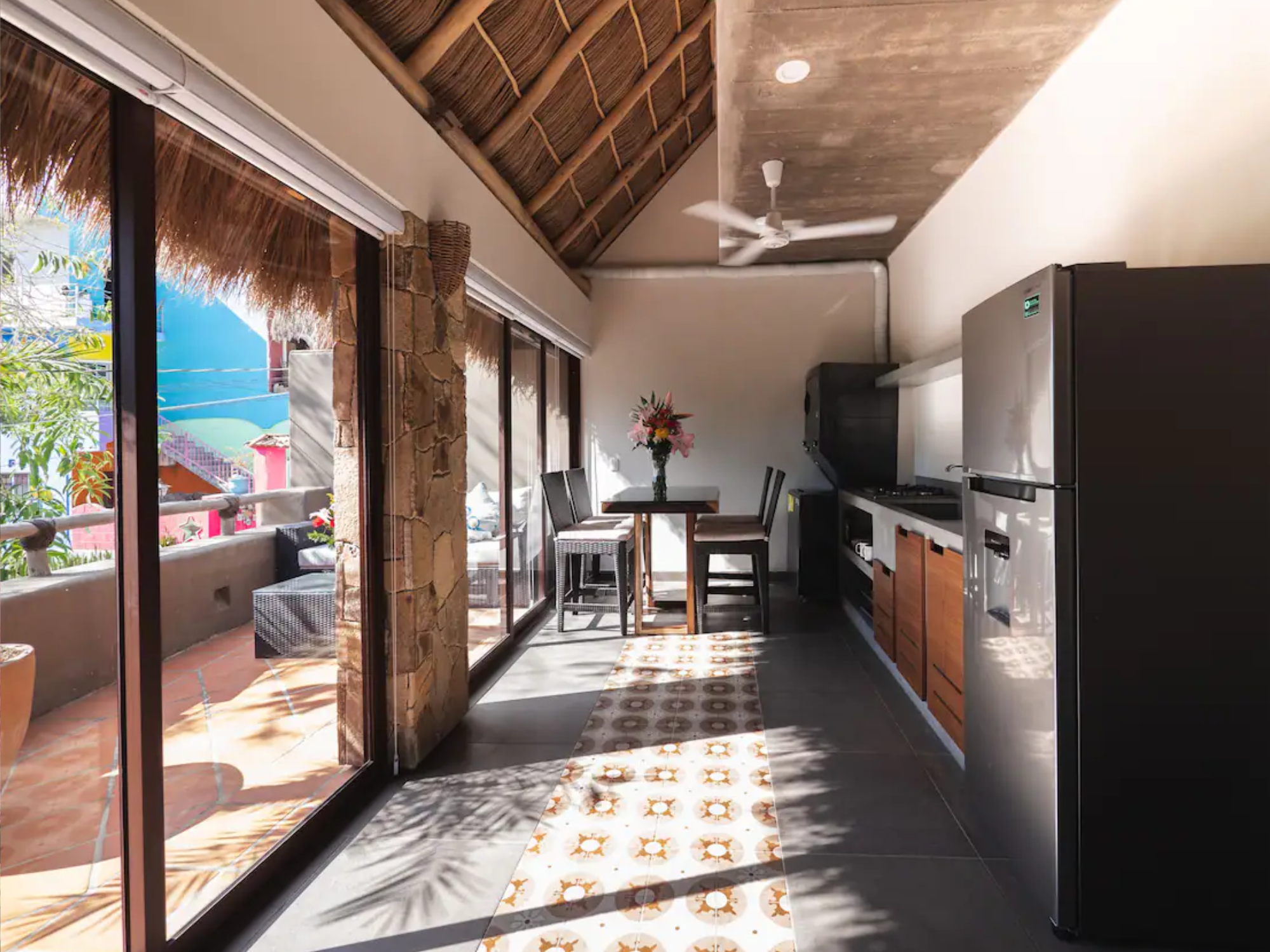 The second kitchen at Villa Vargas Sayulita under a palapa roof, with a gas range, fridge, dining table and sliding doors to the upper terrace