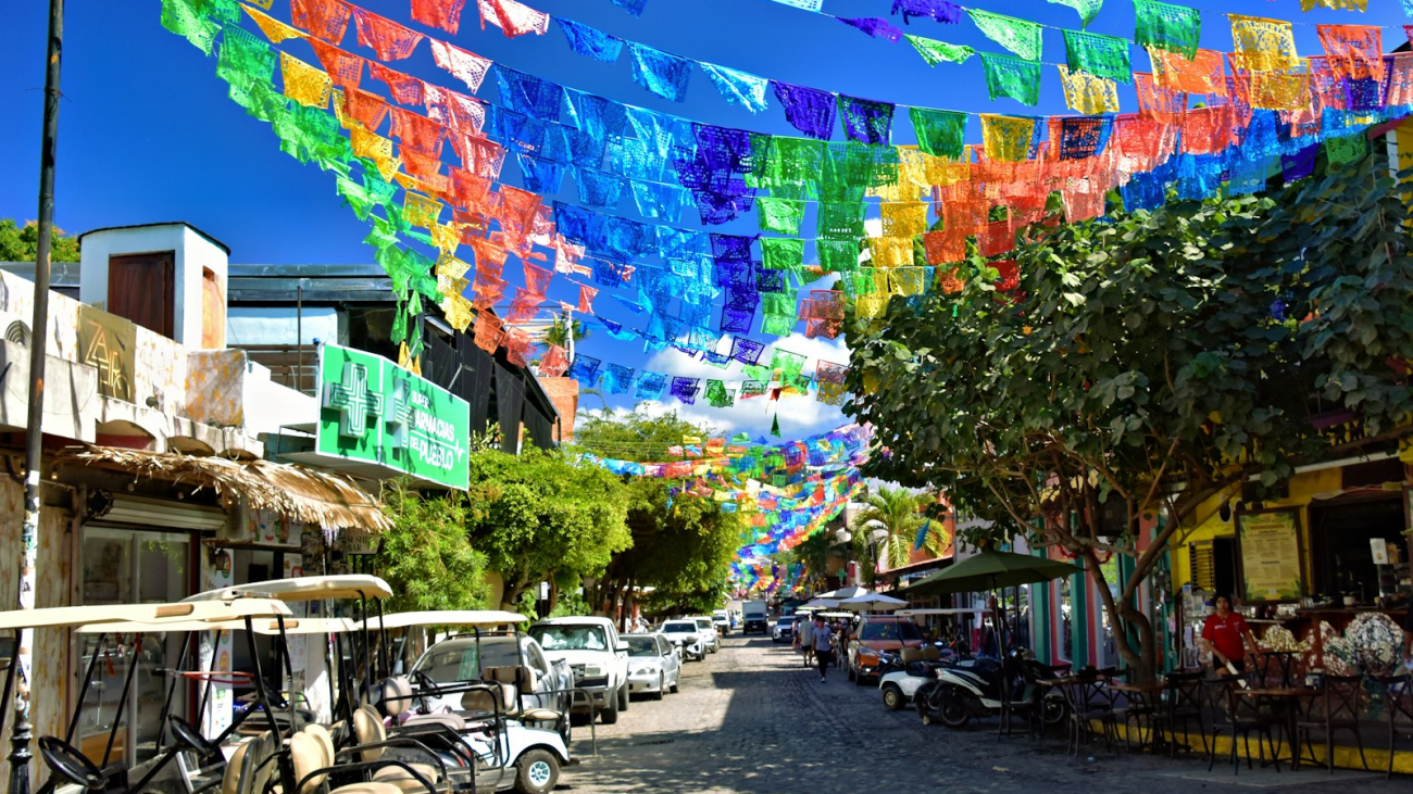 Colorful flags strung across a sunny Mexican street with golf carts, Sayulita Pueblo Magico