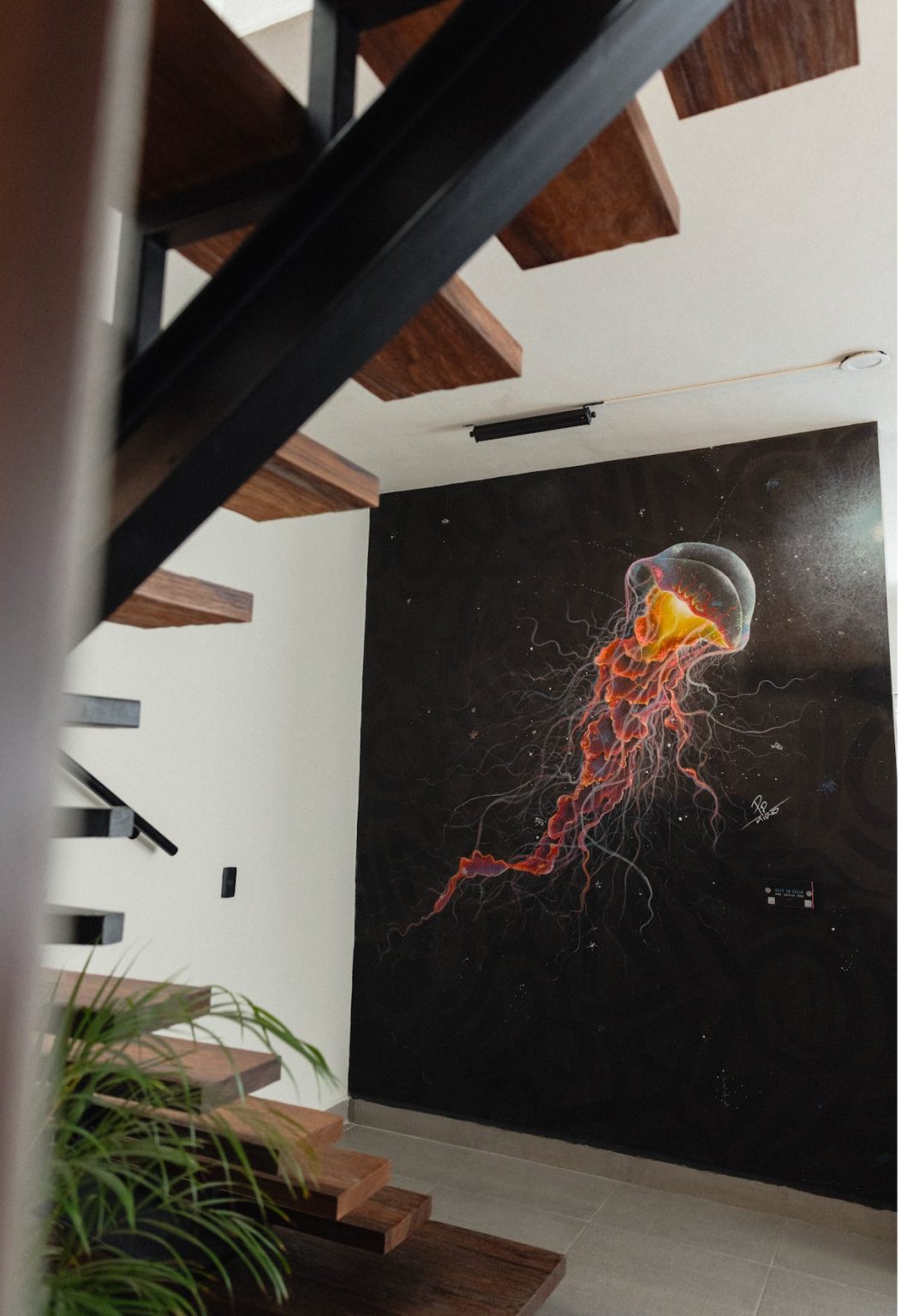 The main-level feature wall at Villa Vargas Sayulita: a life-size jellyfish painted on black by the artist Pepe Niño, seen past the floating Parota staircase