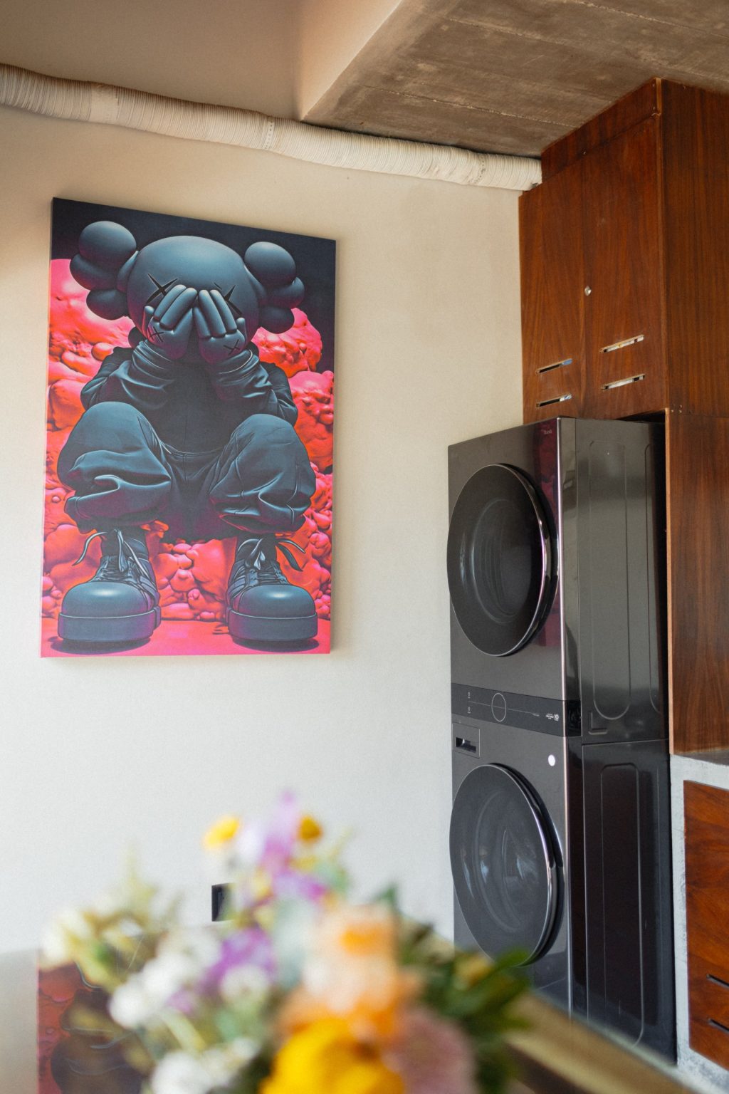 The laundry on the upper level at Villa Vargas Sayulita: a stacked washer and dryer built into hardwood cabinetry, with a large artwork on the wall beside it