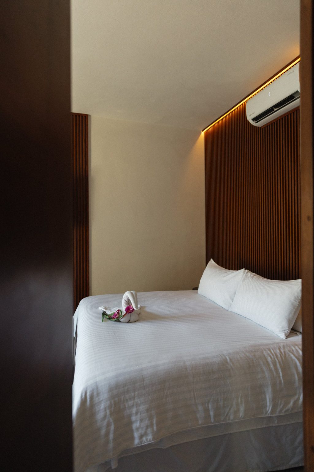 The master bedroom at Villa Vargas Sayulita seen through its doorway, the king bed and the backlit slatted headboard wall framed by the door surround