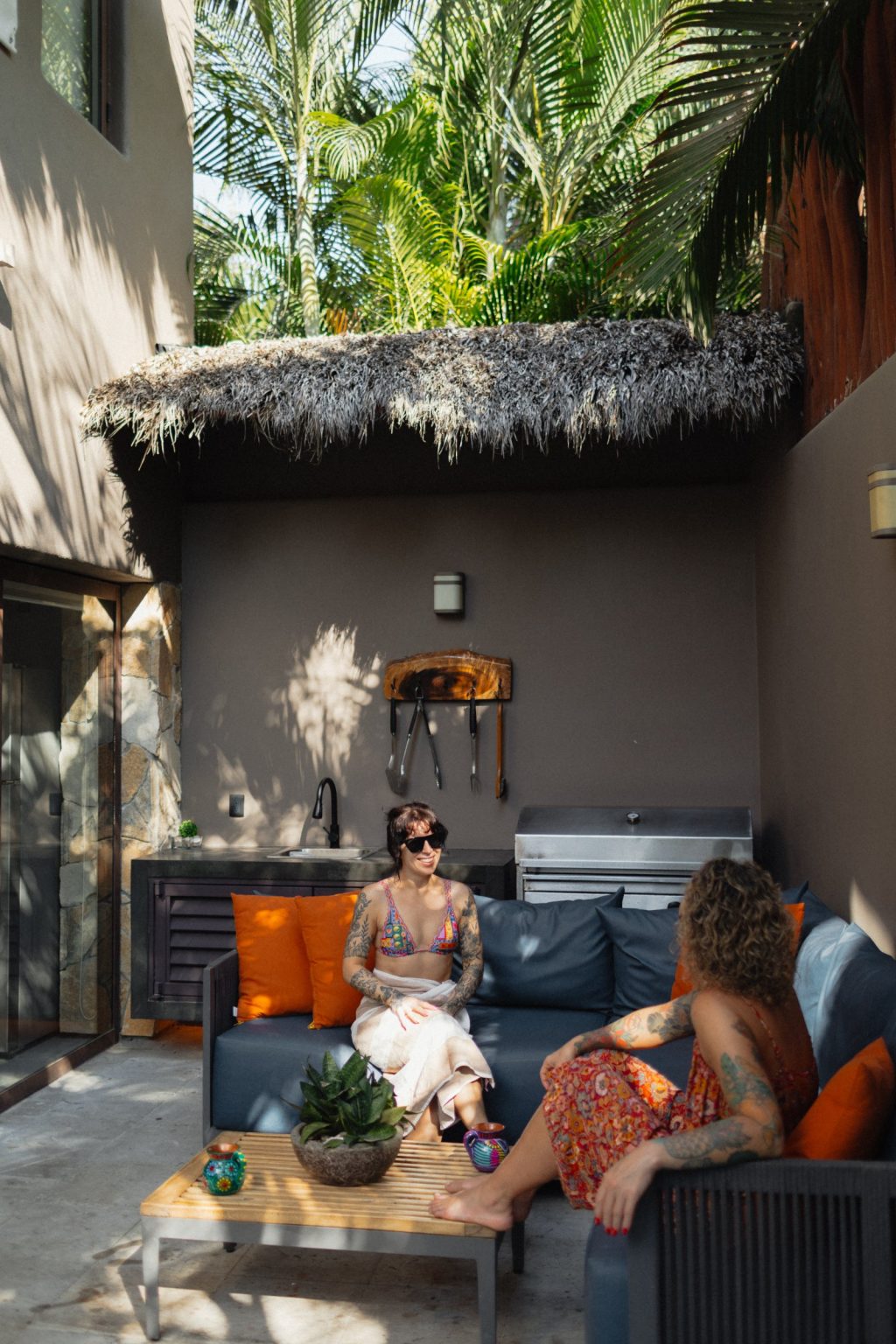 The outdoor kitchen at Villa Vargas Sayulita under a palapa roof, with a sink, concrete counter, stainless BBQ grill and barbecue tools on a live-edge rack