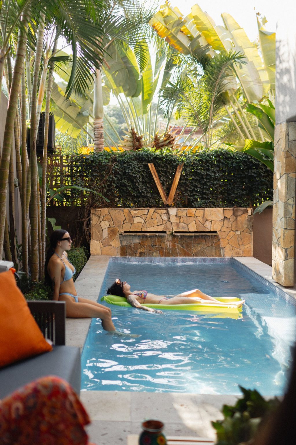 The private pool at Villa Vargas Sayulita in daylight with water running down the stone waterfall wall and the villa mark set into the hedge above