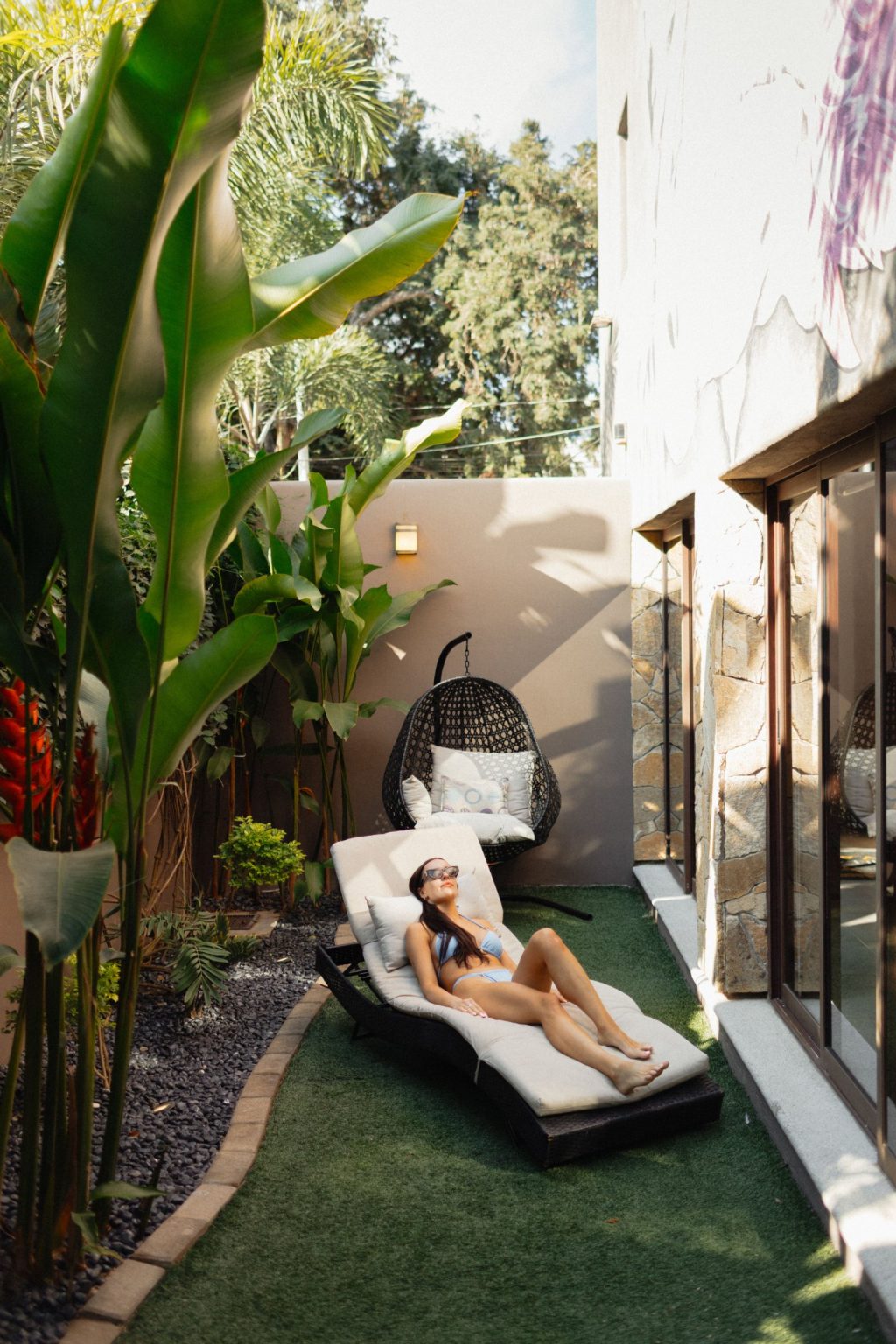 The sheltered sun deck at Villa Vargas Sayulita, with a cushioned lounger and a hanging chair beside the sliding glass doors and tropical planting